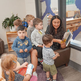 A group of children listen to an educator read a book to them in a classroom.