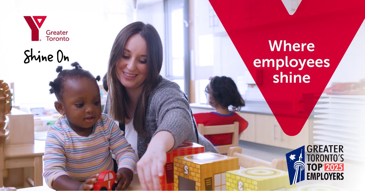 A smiling early child care educator encourages a child playing in a YMCA child care centre.