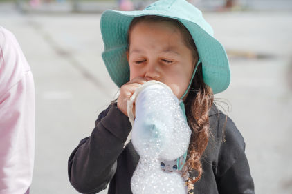 A child in a blue sun hat and black top blows bubbles.