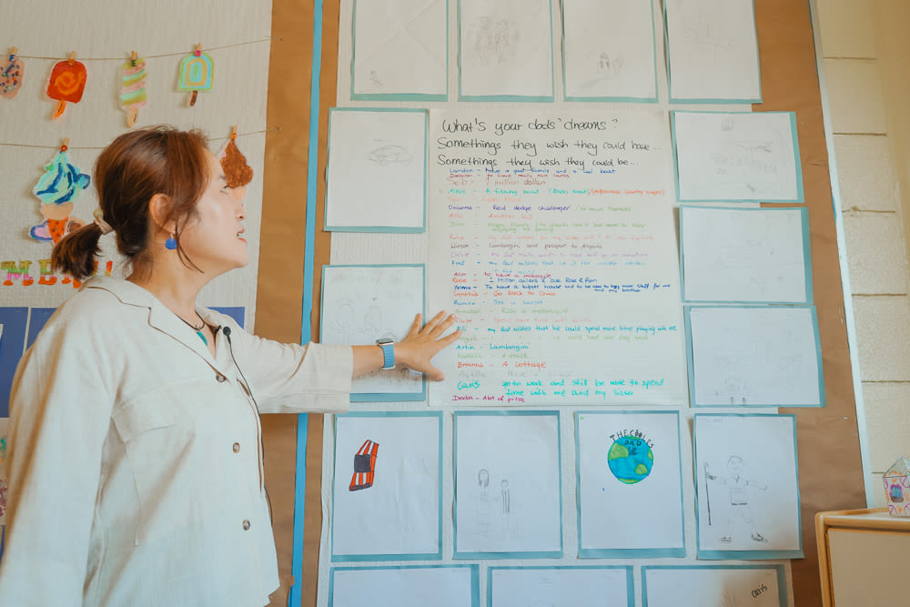 Jenny points to a wall adorned with drawings made by the children to celebrate Father's Day.