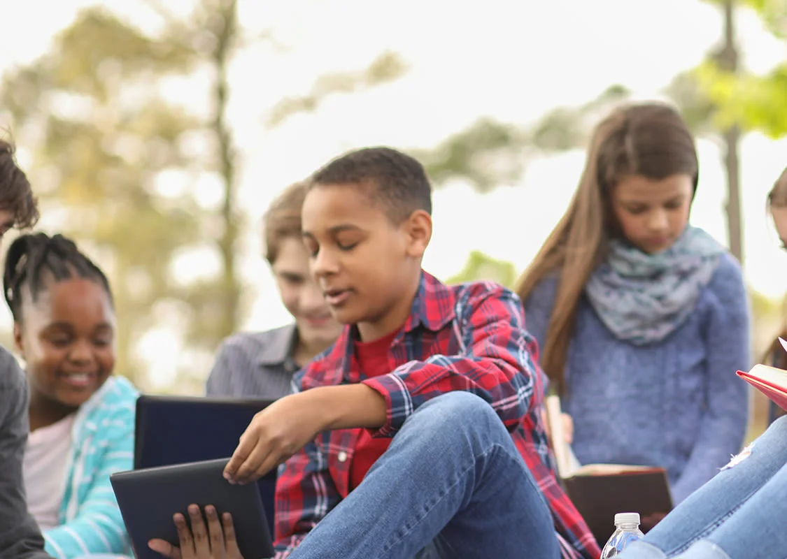 Middle school students reading from books and devices in the park