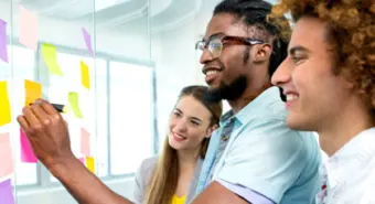 A group of three youth writing on post-it notes on the wall