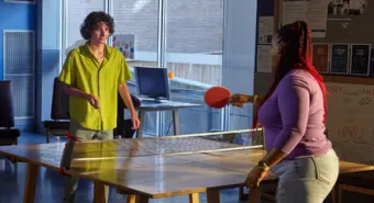 A youth plays ping pong with a staff member in a YMCA shelter.