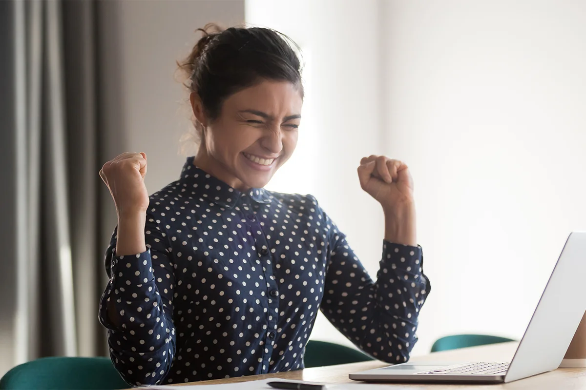 a woman pumping her fists in success in front of a computer