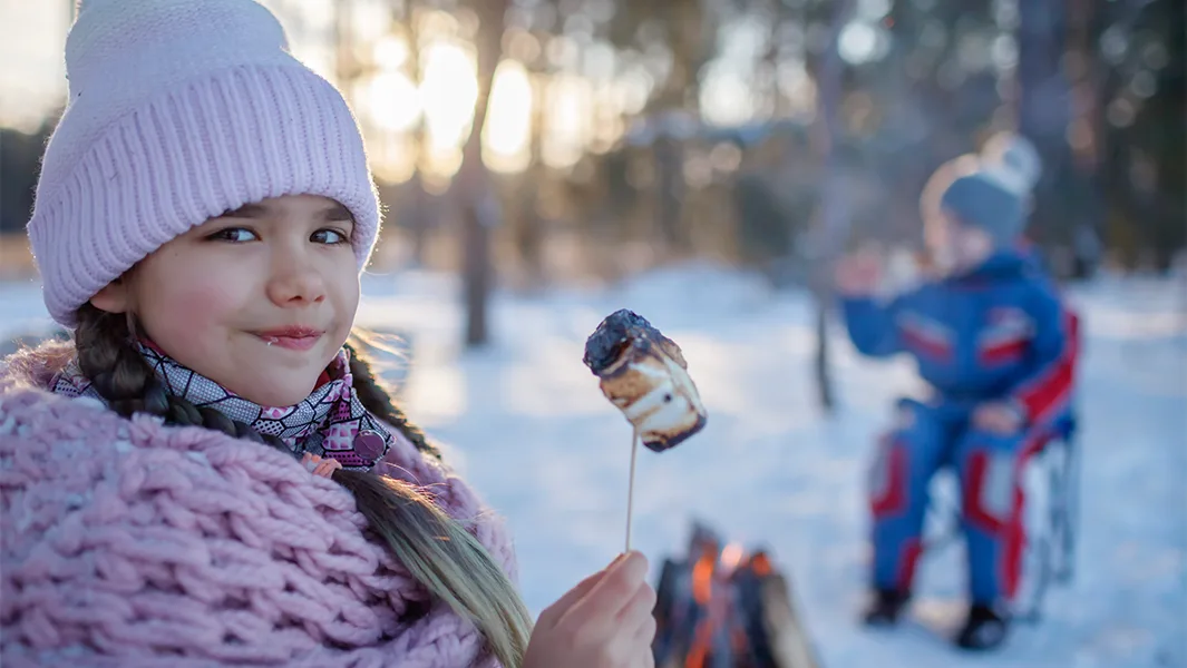 Girl eating a roasted marshmallow by camp fire in winter