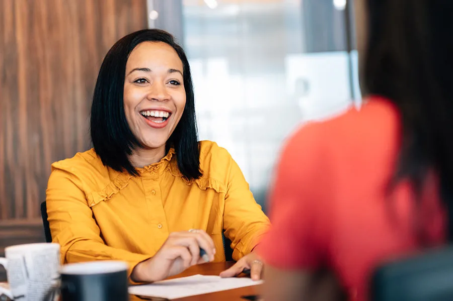 a woman talking to another woman over a table, smiling