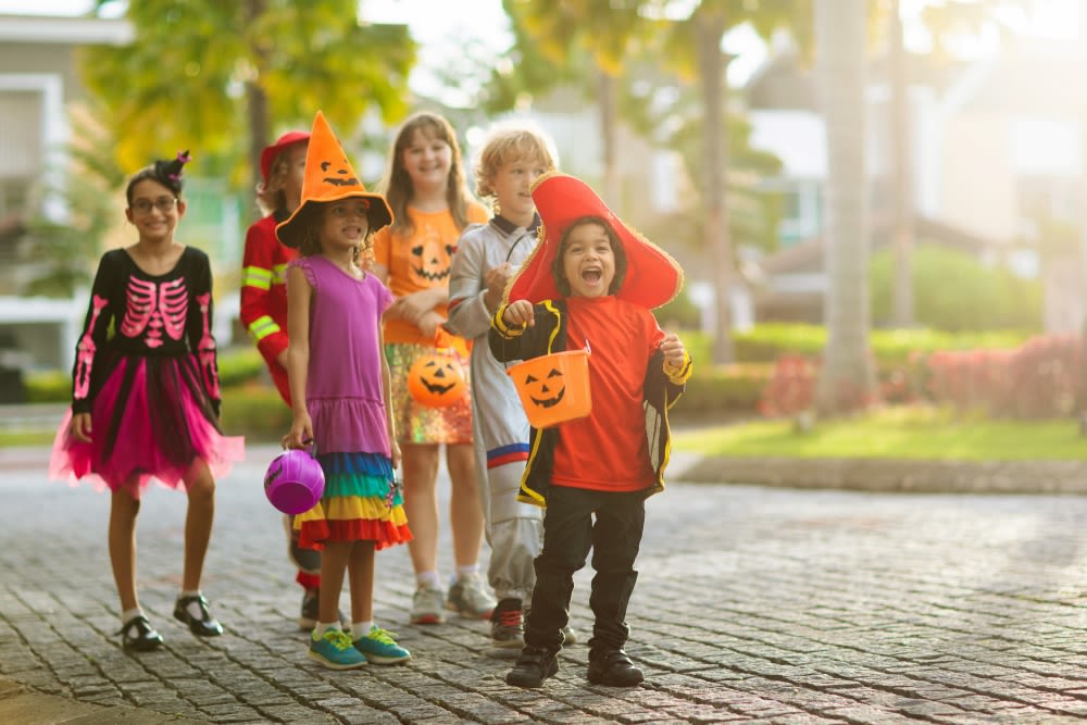 A group of children in Halloween costumes trick-or-treat on a sidewalk.