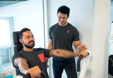 Man bench pressing on a machine and personal trainer helping coach him