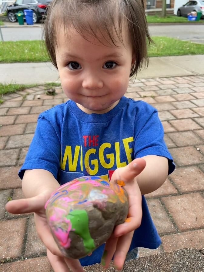 A little girl holding out her hands with a painted rock 