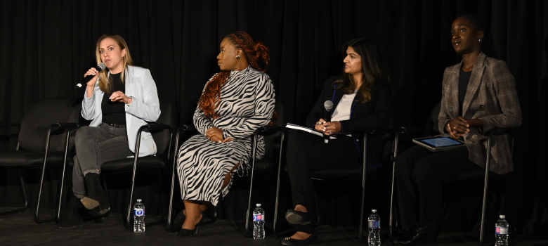 A panelist speaks into a microphone while three other panelists listen