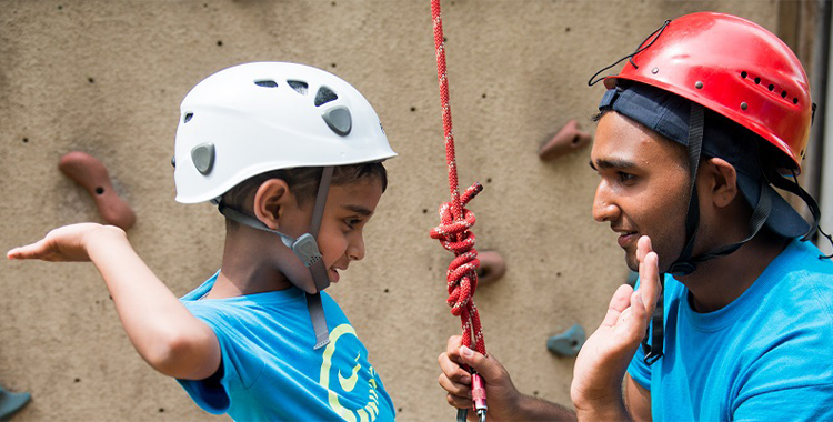 A child about to hand five a Y camp counsellor at a rock climbing wall